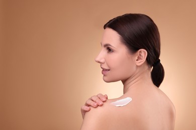 Photo of Beautiful woman with smear of body cream on her shoulder against light brown background. Space for text