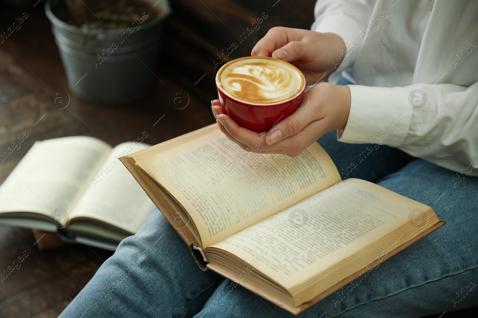 Photo of Woman with cup of coffee reading book indoors, closeup