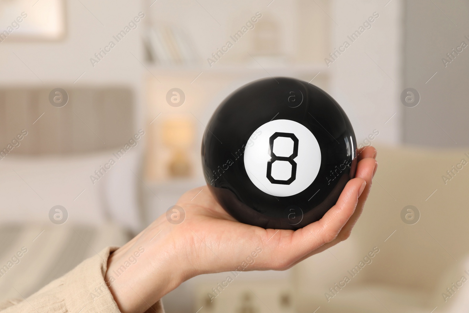 Photo of Woman holding magic eight ball indoors, closeup