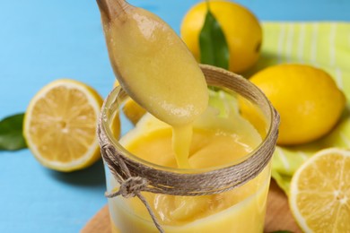 Taking delicious lemon curd from jar at light blue table, closeup