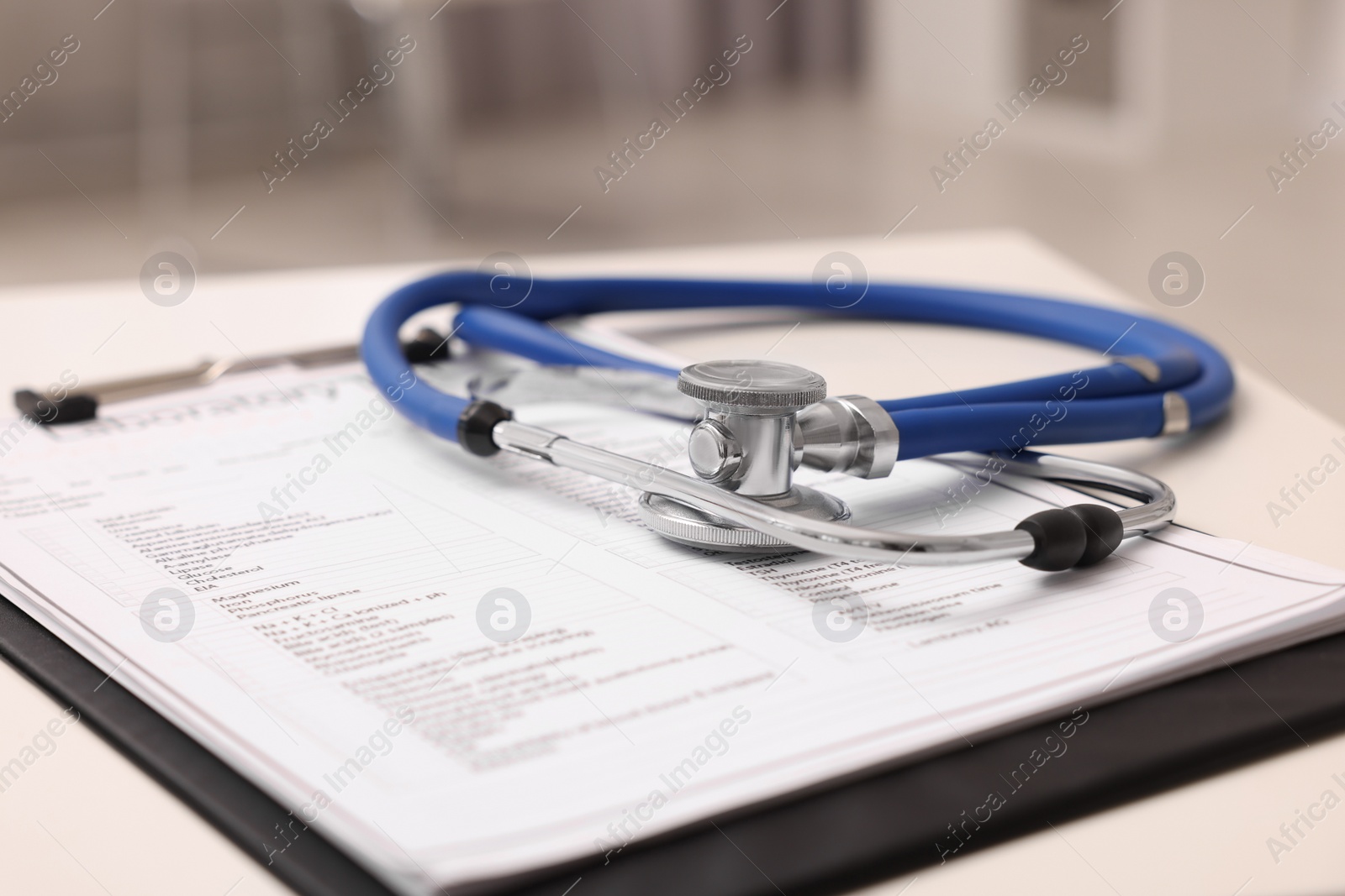 Photo of Clipboard and stethoscope on white table in clinic, closeup. Doctor's workplace