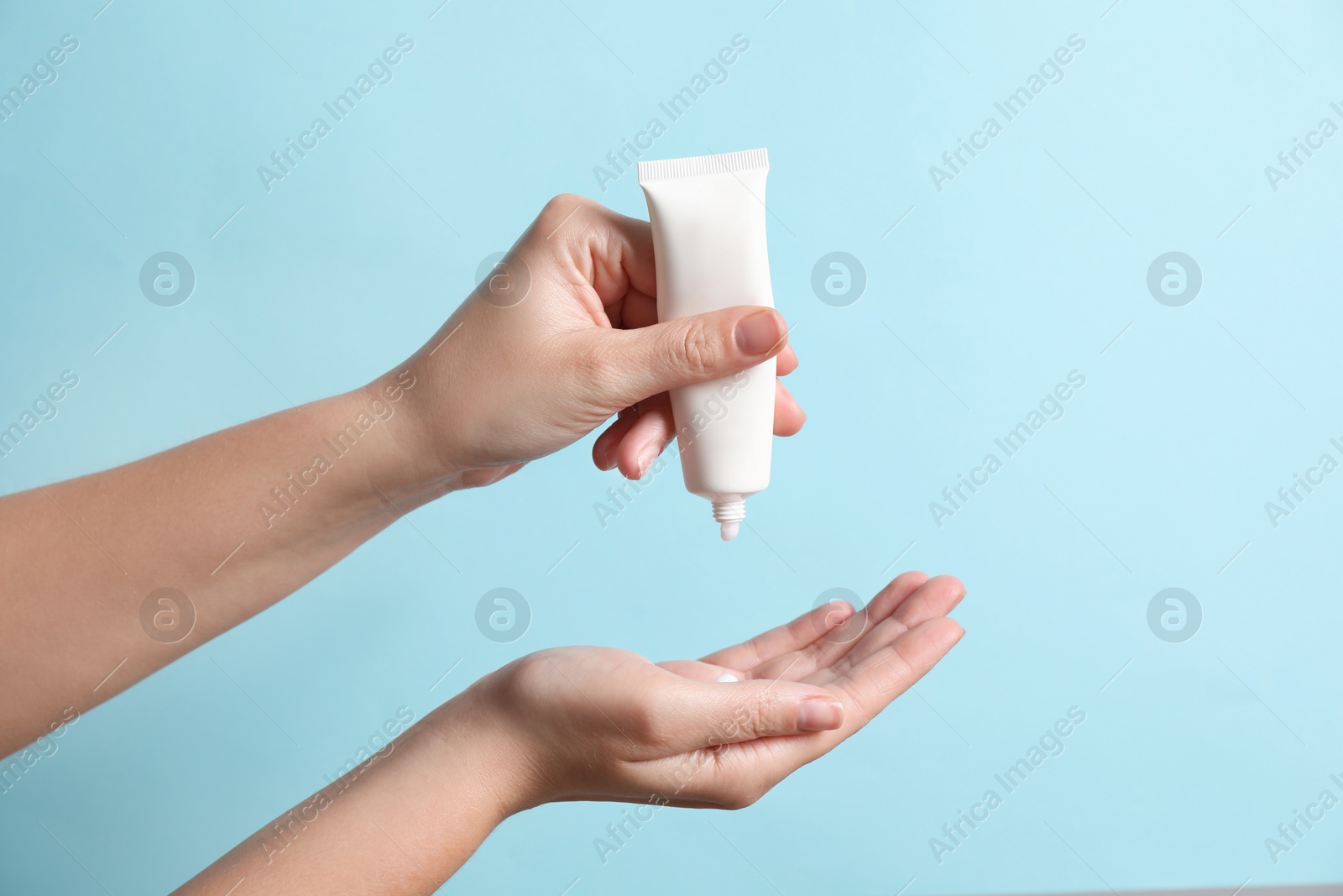 Photo of Woman applying cosmetic cream from tube onto her hand on light blue background, closeup