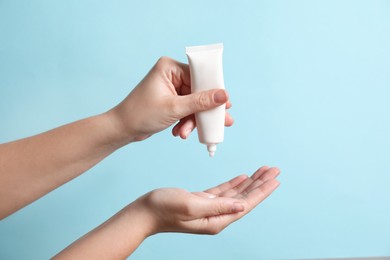 Photo of Woman applying cosmetic cream from tube onto her hand on light blue background, closeup