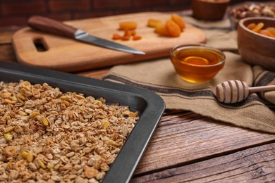 Making granola. Baking tray with mixture of oat flakes and other ingredients on wooden table