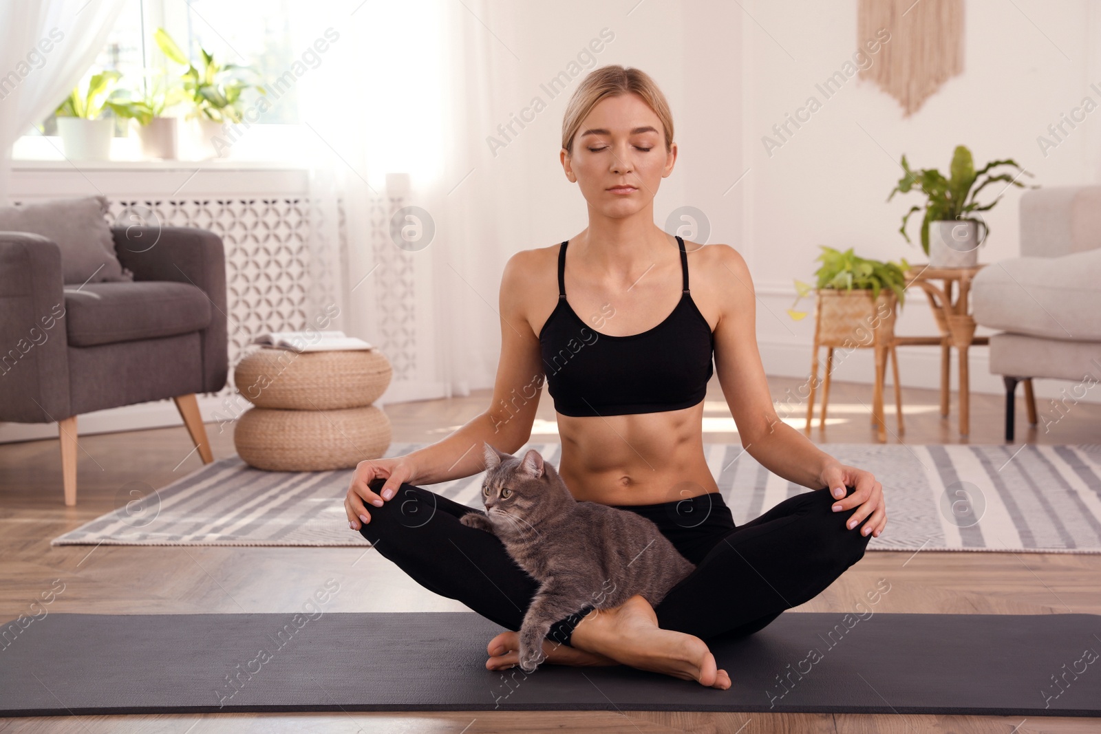 Photo of Beautiful woman with cat practicing yoga at home