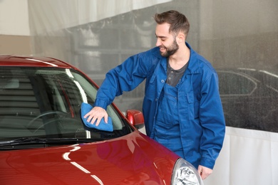 Worker cleaning automobile windshield with rag at car wash
