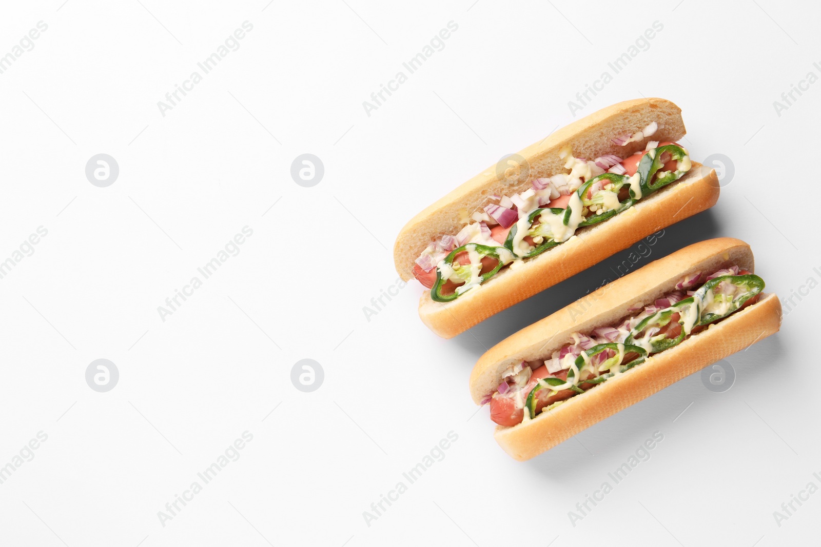 Photo of Delicious hot dogs with onion, chili pepper and sauce on white background, flat lay. Space for text