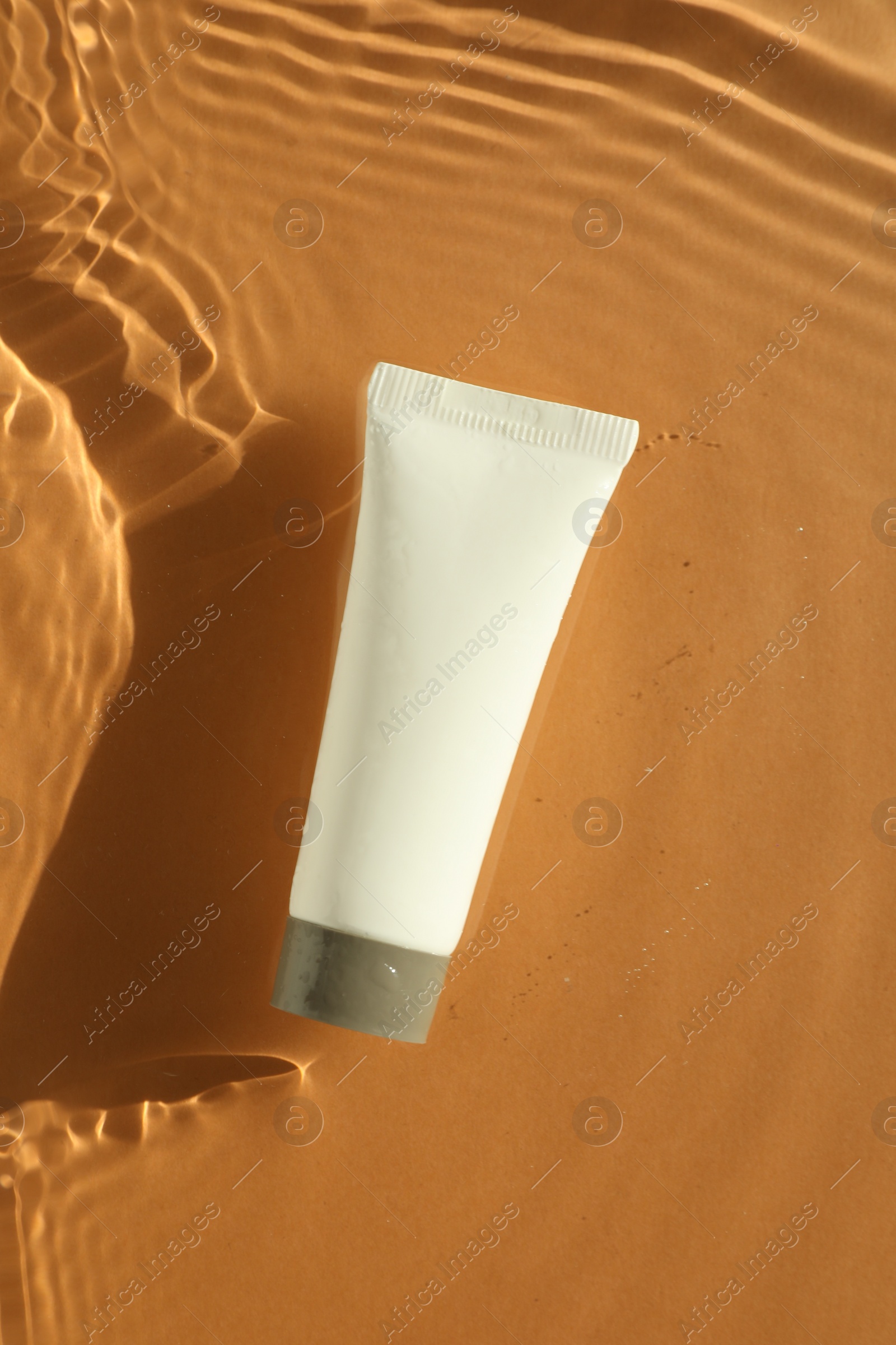 Photo of Tube with moisturizing cream in water on orange background, top view