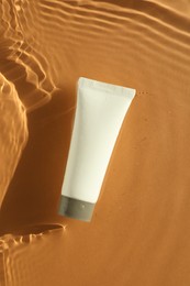 Tube with moisturizing cream in water on orange background, top view