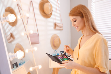 Beautiful young woman applying makeup near mirror in dressing room