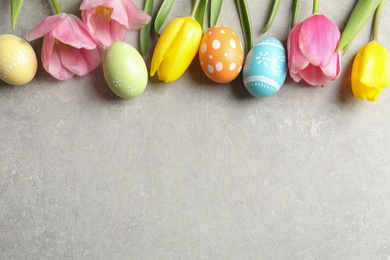 Photo of Flat lay composition of painted Easter eggs and flowers on color background, space for text