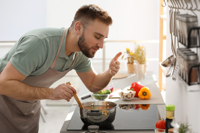 Young man cooking delicious soup in kitchen