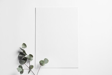 Photo of Empty sheet of paper and decorative eucalyptus leaves on white background, flat lay. Mockup for design