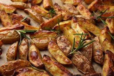 Tasty baked potato and aromatic rosemary on parchment paper, closeup