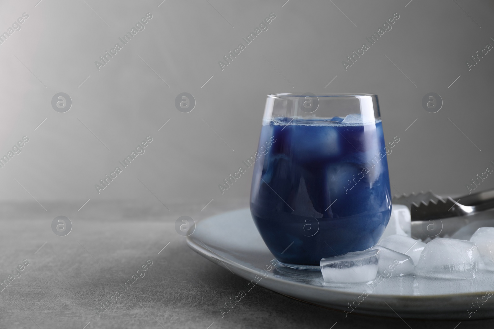 Photo of Delicious blue matcha tea with ice cubes on grey table, space for text