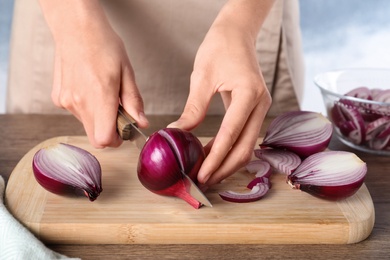 Photo of Young woman cutting ripe red onion on board at wooden table, closeup
