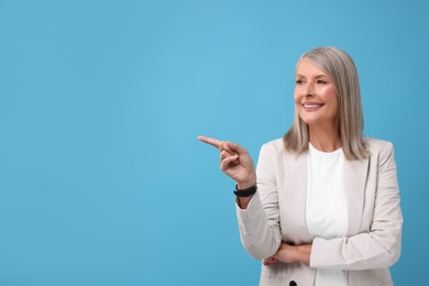 Photo of Portrait of beautiful middle aged woman pointing at something on light blue background, space for text