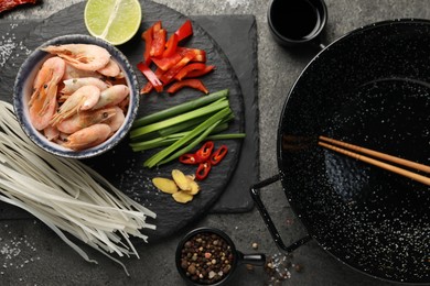 Flat lay composition with black wok, spices and products on dark textured table