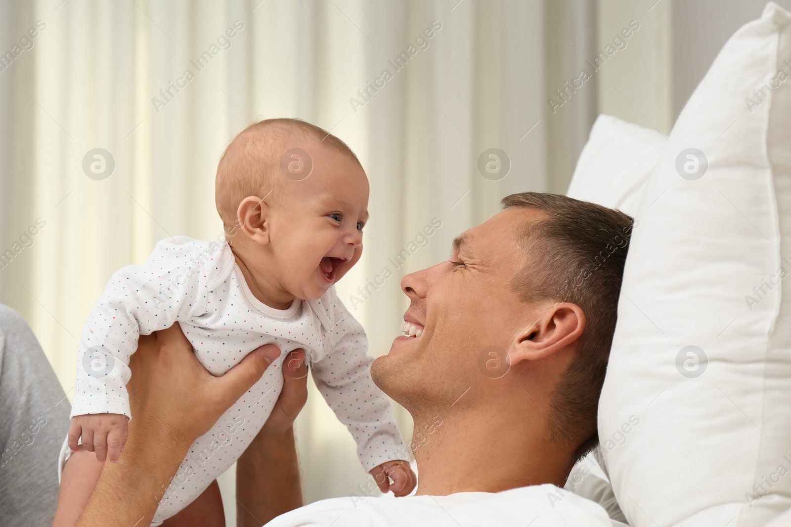 Photo of Happy father holding his cute baby on bed at home
