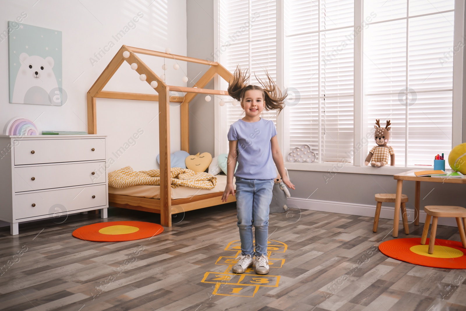 Photo of Cute little girl playing hopscotch at home