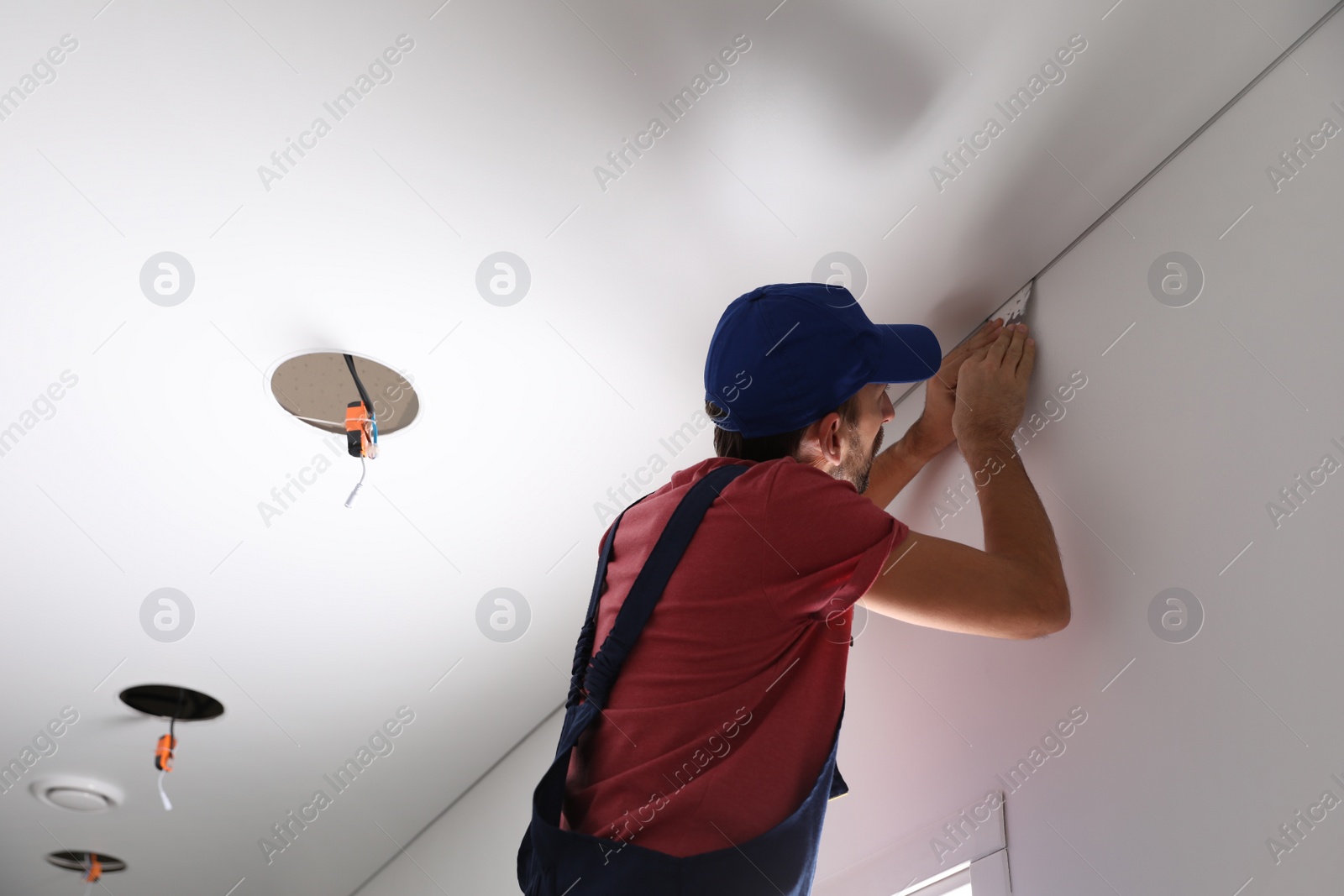 Photo of Worker installing stretch ceiling in empty room