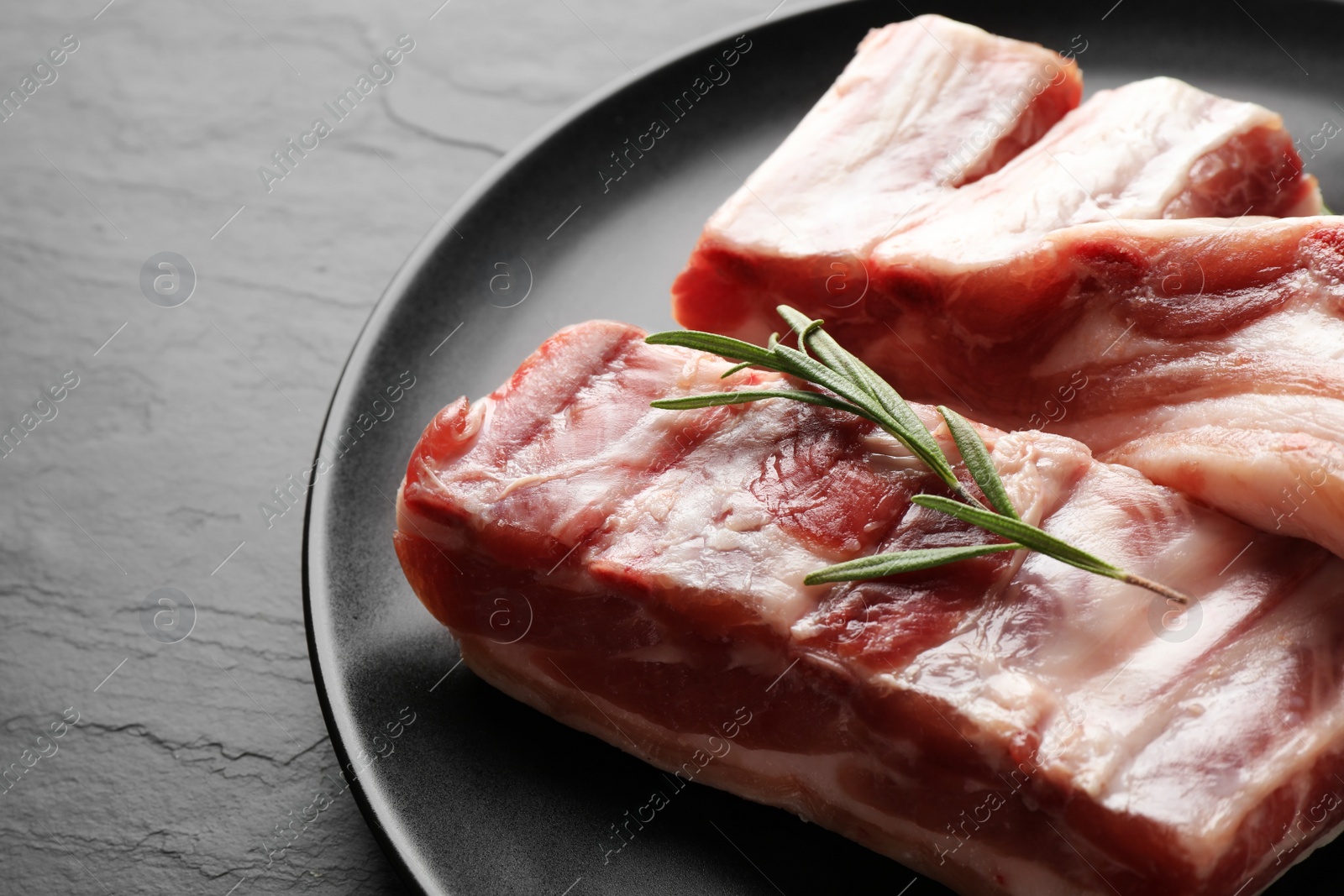 Photo of Raw ribs with rosemary on black table, closeup