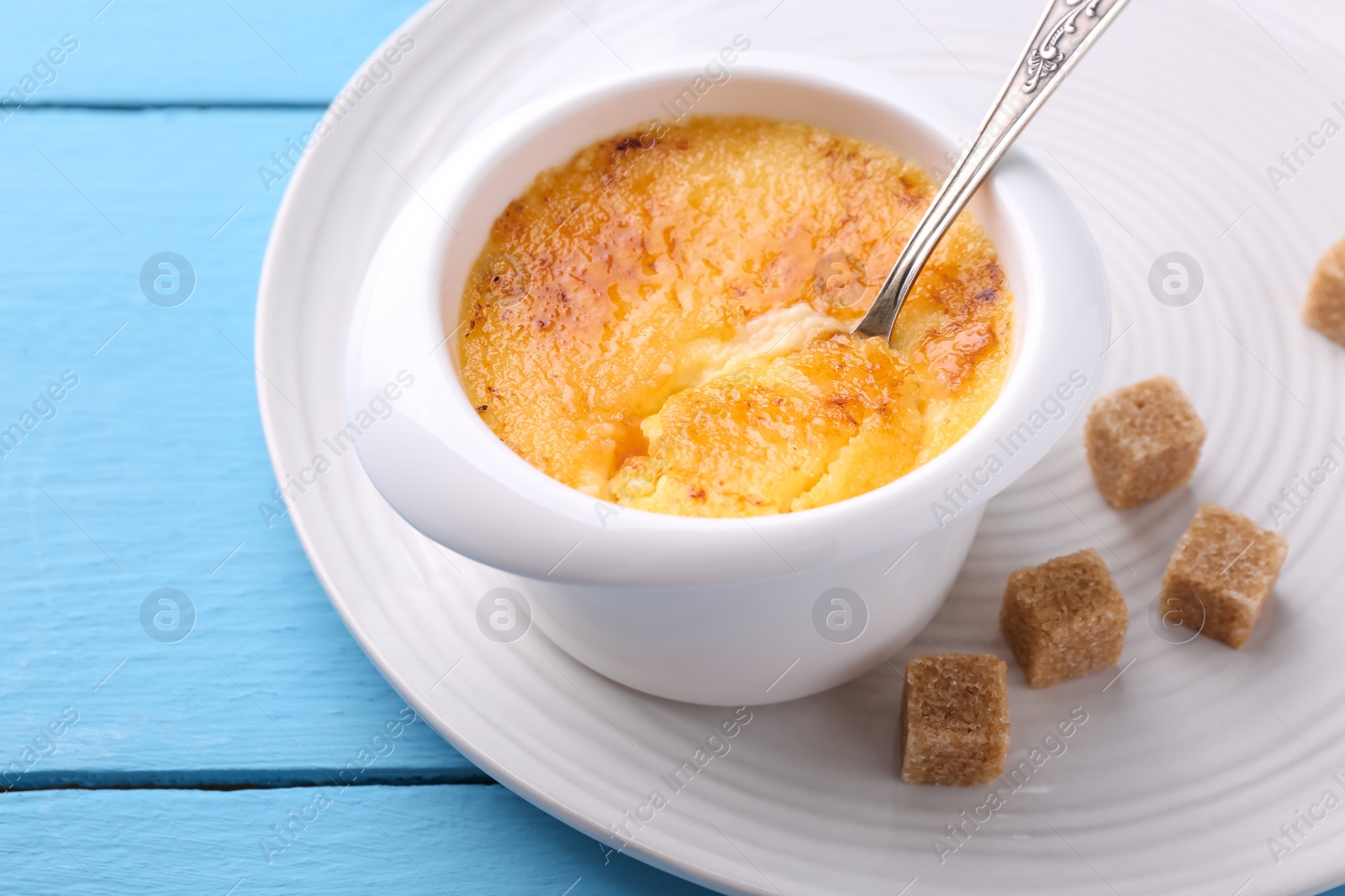 Photo of Delicious creme brulee in bowl served on light blue wooden table, closeup