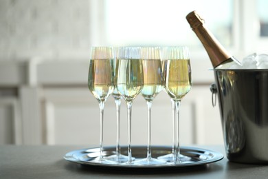 Glasses of champagne and ice bucket with bottle on grey table