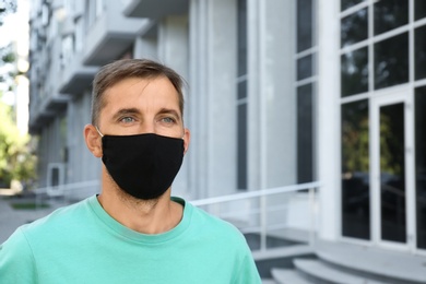 Photo of Man wearing handmade cloth mask outdoors, space for text. Personal protective equipment during COVID-19 pandemic