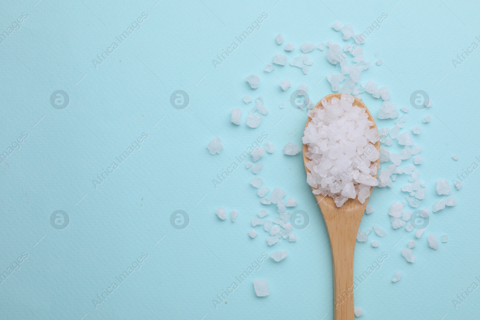 Photo of Spoon with sea salt on light blue background, top view. Space for text