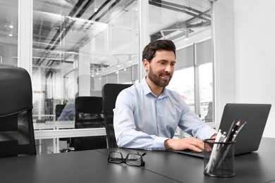 Man working on laptop at black desk in office. Space for text