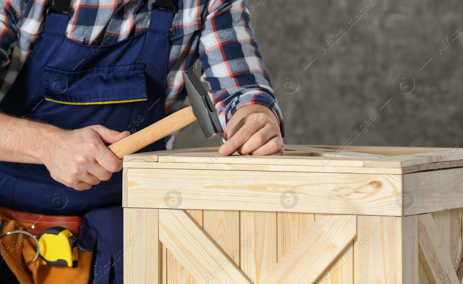 Photo of Working man hammering nail into wooden crate indoors, closeup