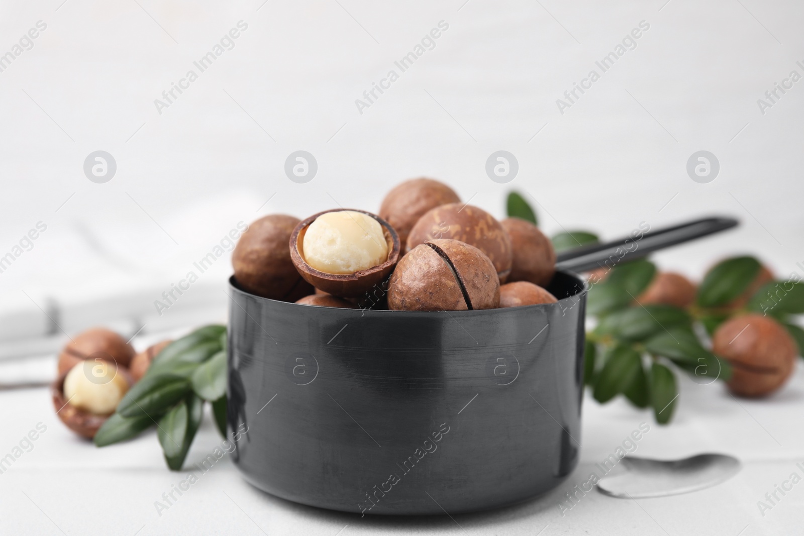 Photo of Tasty organic Macadamia nuts in small saucepan on white table