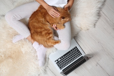 Woman with cute red cat and laptop on fur carpet, top view