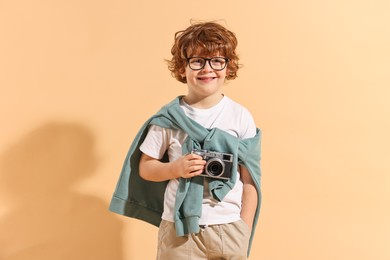 Photo of Fashion concept. Stylish boy with vintage camera on pale orange background