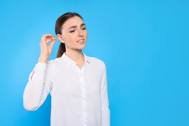 Photo of Young woman cleaning ear with cotton swab on light blue background. Space for text