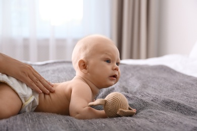 Young woman massaging cute little baby on bed at home