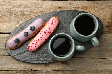 Aromatic coffee in cups and tasty eclairs on wooden table, top view