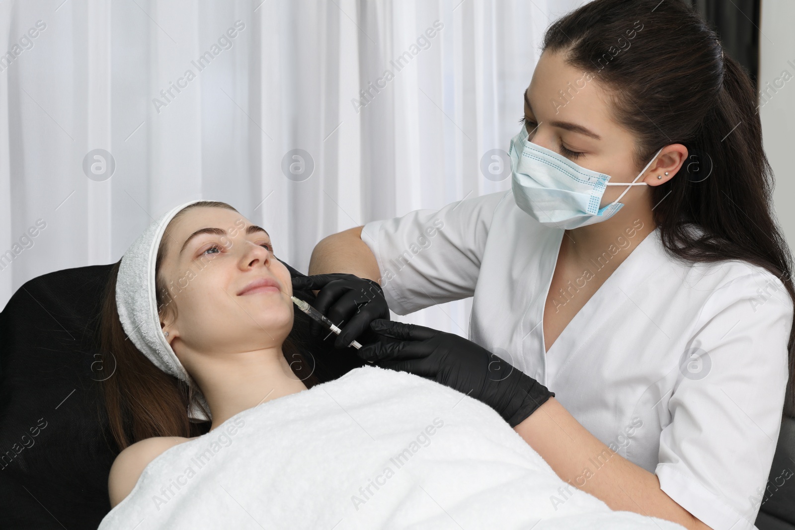 Photo of Cosmetologist giving lips injection to patient in clinic. Cosmetic surgery