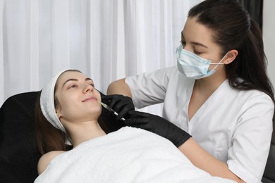 Photo of Cosmetologist giving lips injection to patient in clinic. Cosmetic surgery