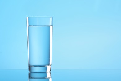 Photo of Glass of water on light blue background. Space for text