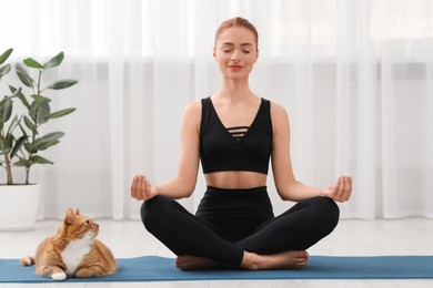 Photo of Beautiful woman with cute red cat practicing yoga on mat at home