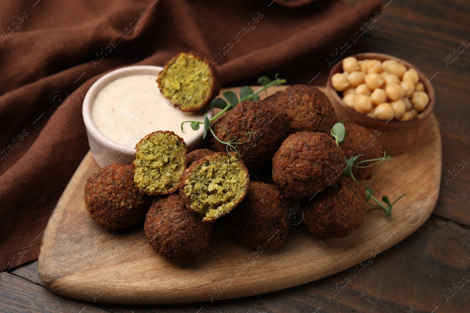 Photo of Delicious falafel balls, chickpeas and sauce on wooden table