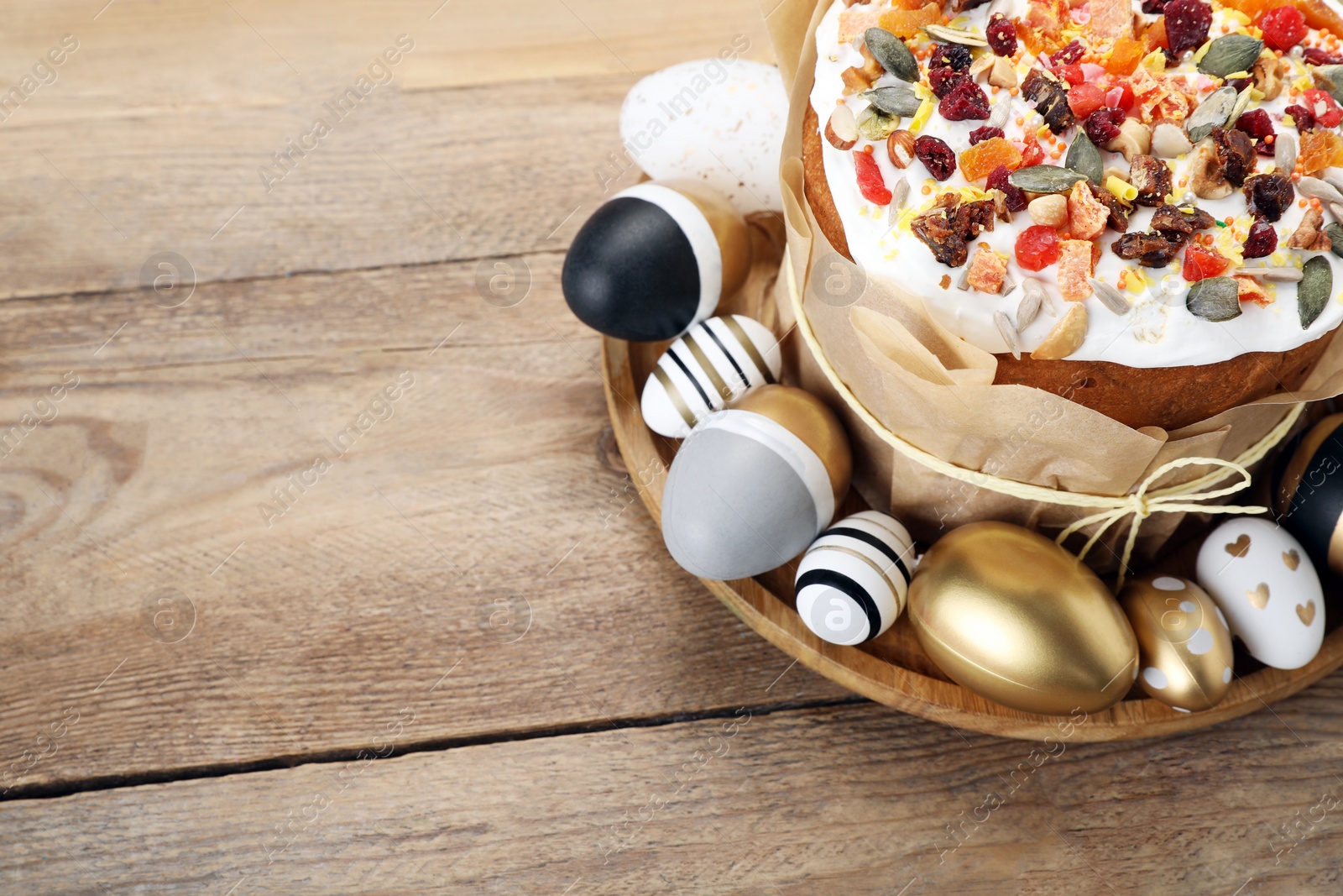 Photo of Traditional Easter cake with dried fruits and painted eggs on wooden table, above view. Space for text