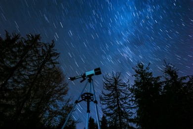 Photo of Modern telescope and beautiful sky in night outdoors, low angle view. Star trail