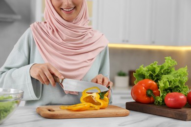 Photo of Muslim woman making delicious salad with vegetables at white table in kitchen, closeup