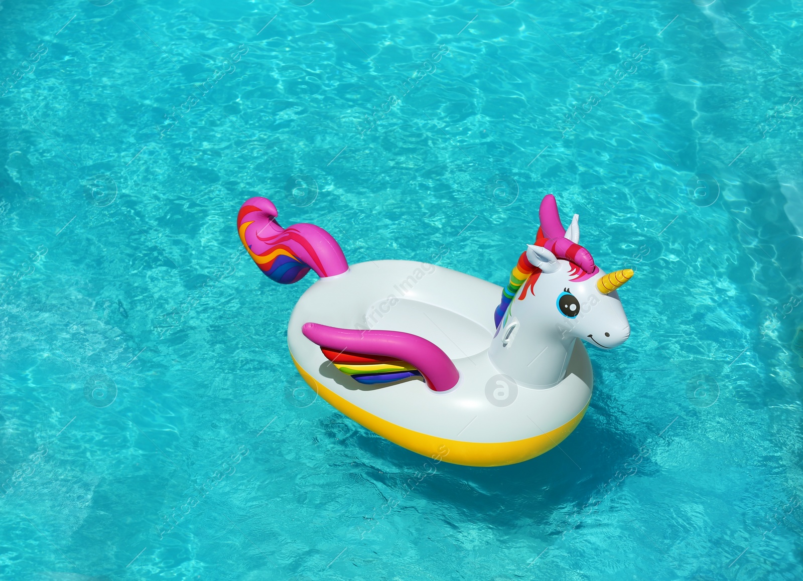 Photo of Funny inflatable unicorn ring floating in swimming pool on sunny day. Space for text