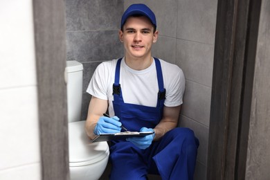 Smiling plumber writing results of examining toilet bowl in water closet