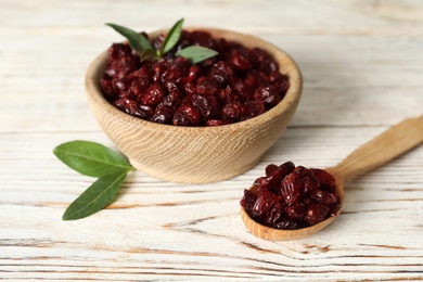 Tasty dried cranberries and leaves on white wooden table