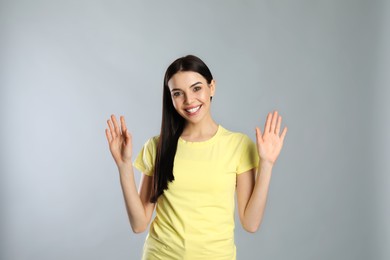 Photo of Attractive young woman showing hello gesture on grey background